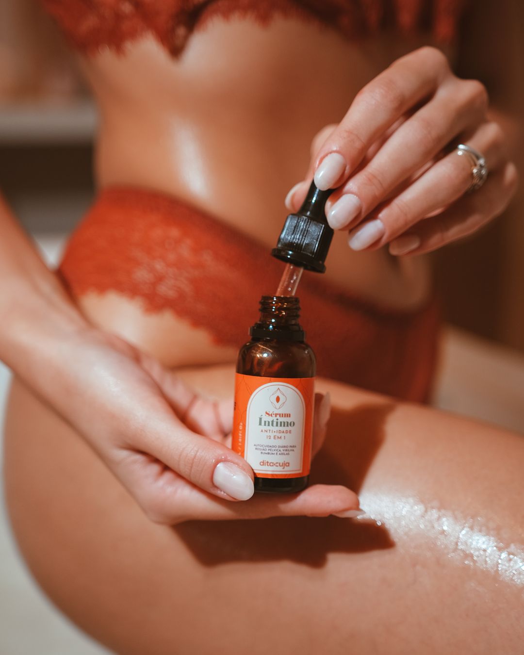 Corpo feminino ao fundo e mãos segurando o Sérum Íntimo e o abrindo