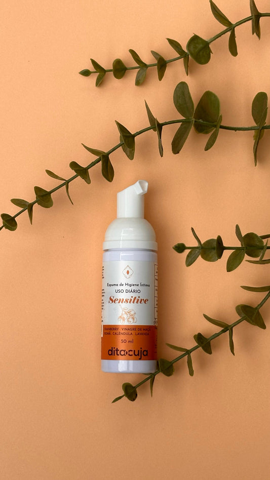 » Mini Espuma Natural de Higiene Sensitive em embalagem branca e laranja em fundo laranja claro e plantas ao lado