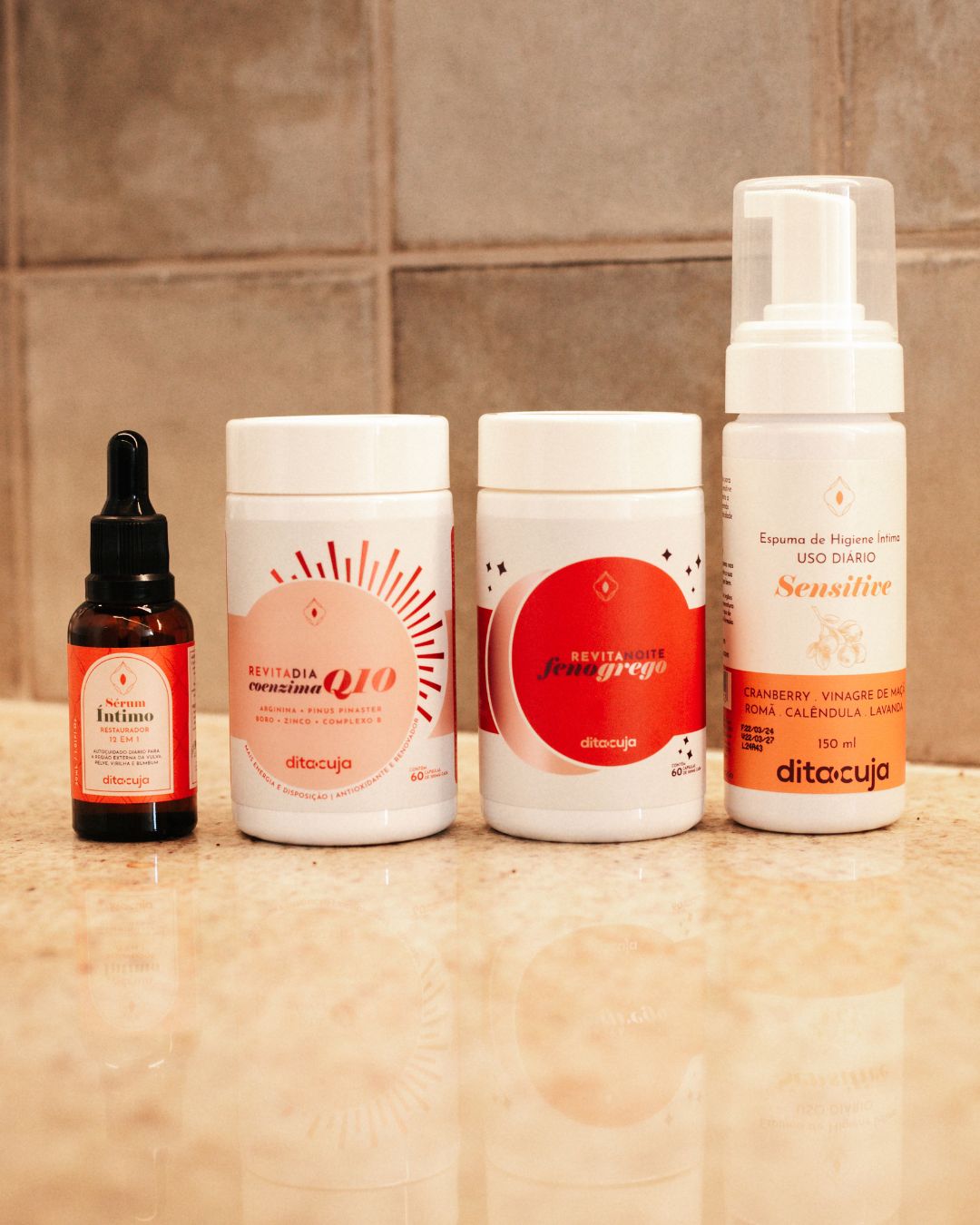 Kit Revitalização Essencial (Revita + Sérum + Espuma) em embalagens em tons avermelhados e rosa claro em cima de mármore e ao fundo azulejos em tons terrosos