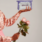 Imagem de mãos femininas segurando necessárie da Ditacuja e rosas